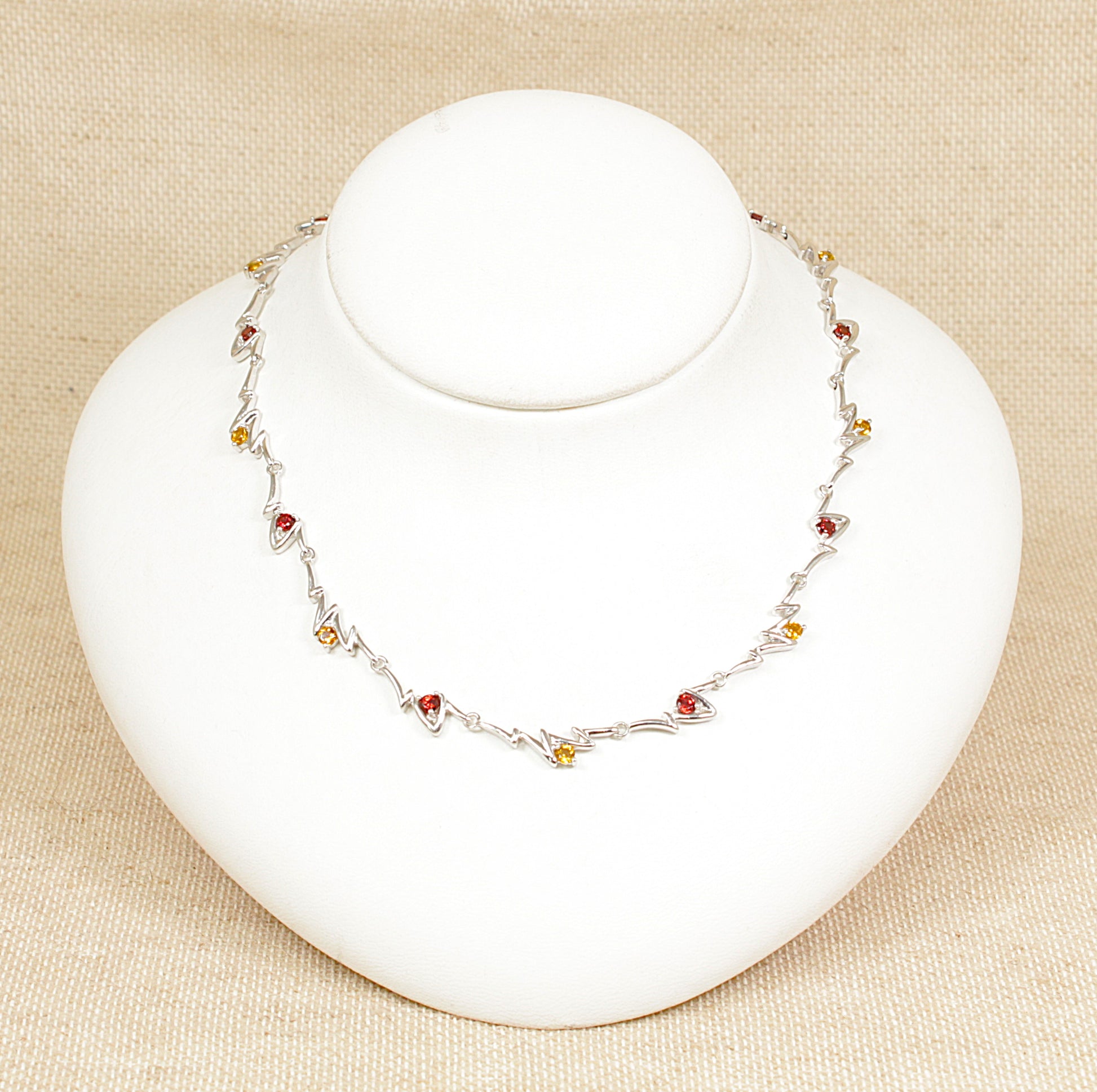 A sterling silver necklace with links set with alternating garnet and citrine gemstones on a white mannequin.