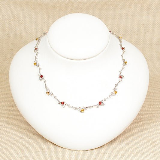 A sterling silver necklace with links set with alternating garnet and citrine gemstones on a white mannequin.
