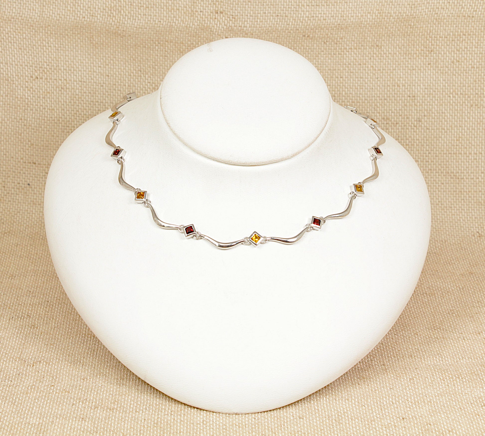 A sterling silver necklace with alternating square bezel-set garnets and citrines, displayed on a white mannequin.