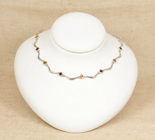 A sterling silver necklace with alternating square bezel-set garnets and citrines, displayed on a white mannequin.