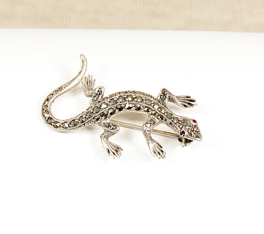 A vintage silver brooch in the shape of a gecko with marcasite stones and ruby-coloured eyes.