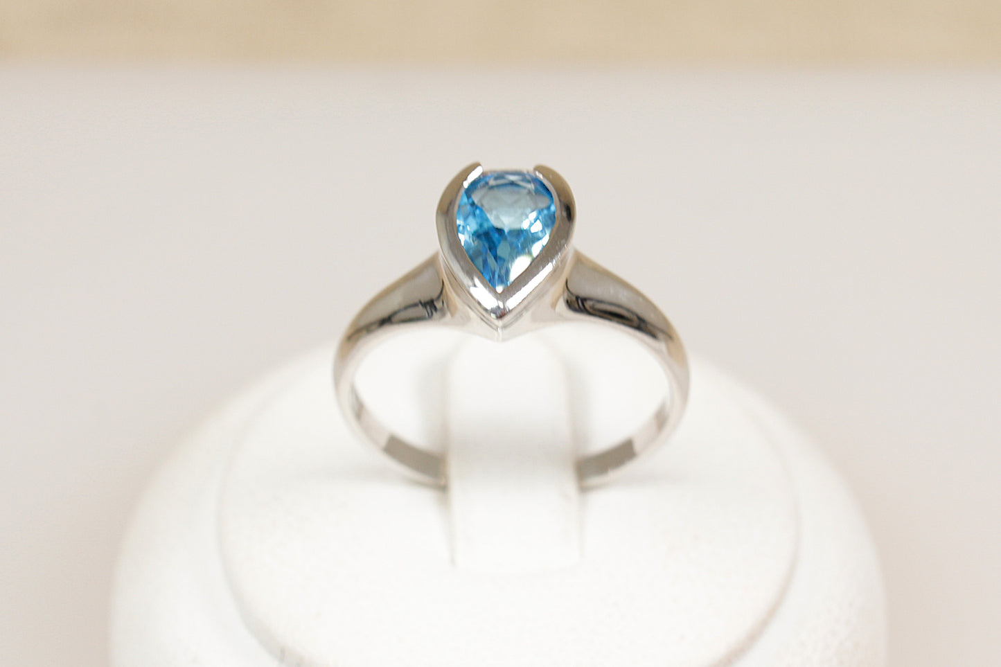 A silver ring with a pear-shaped blue topaz centerpiece set in a bezel, displayed on a white mount.