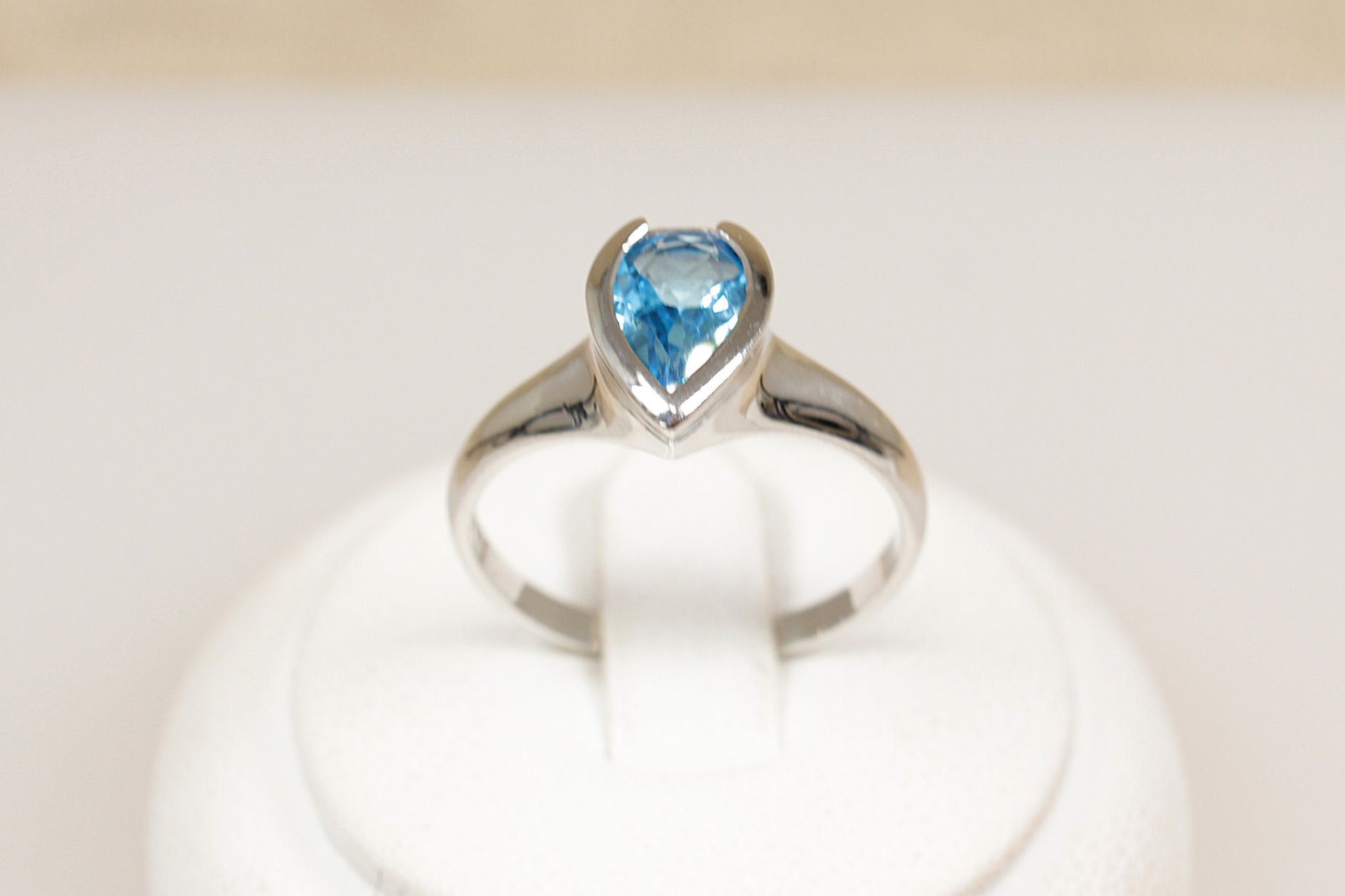 A silver ring with a pear-shaped blue topaz centerpiece set in a bezel, displayed on a white mount.