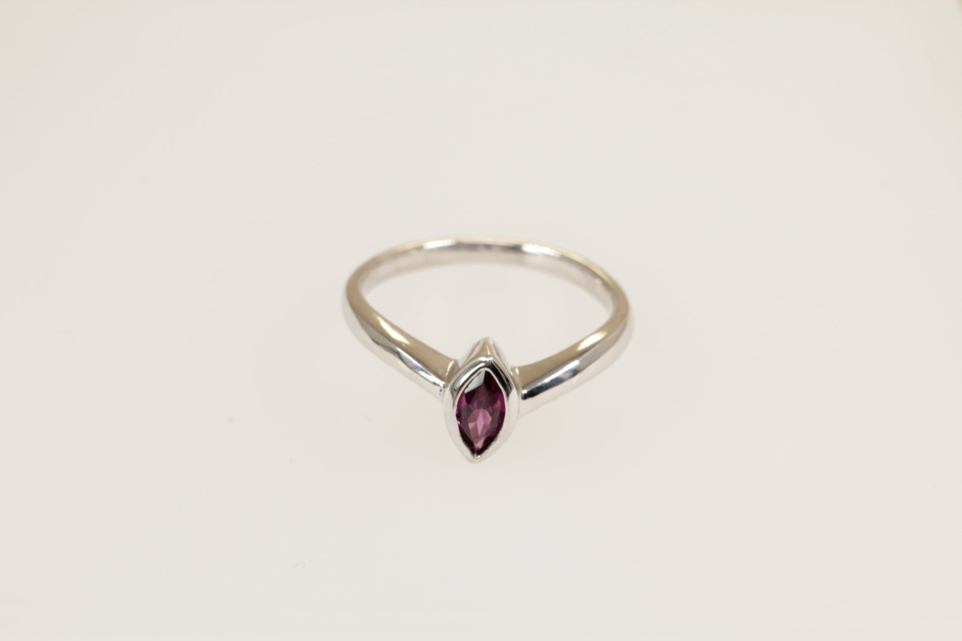 A silver solitaire ring with a marquise cut garnet in a bezel setting, on a plain white background.
