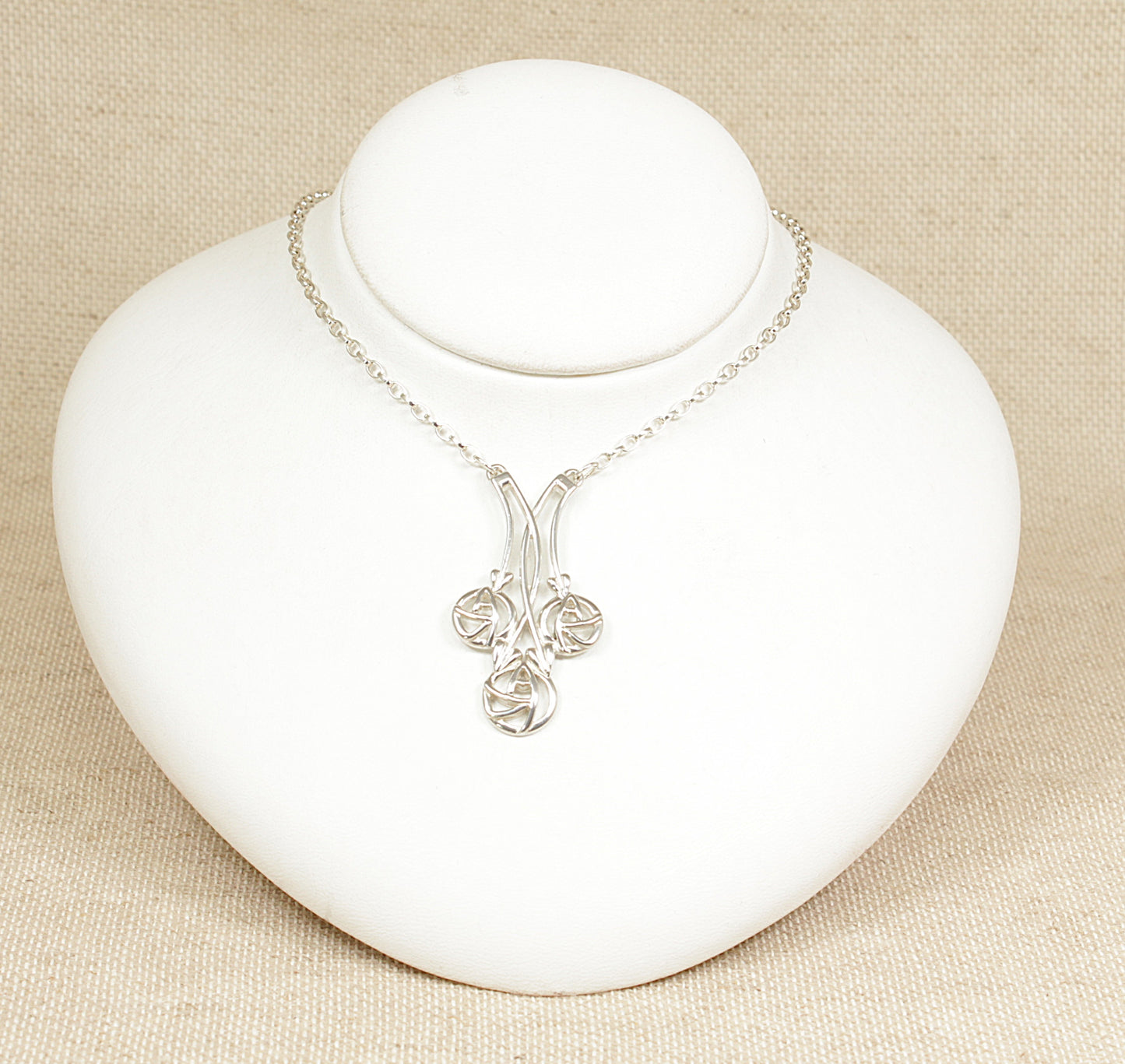 A silver necklet necklace with a geometric and floral design pendant, displayed on a white mannequin.