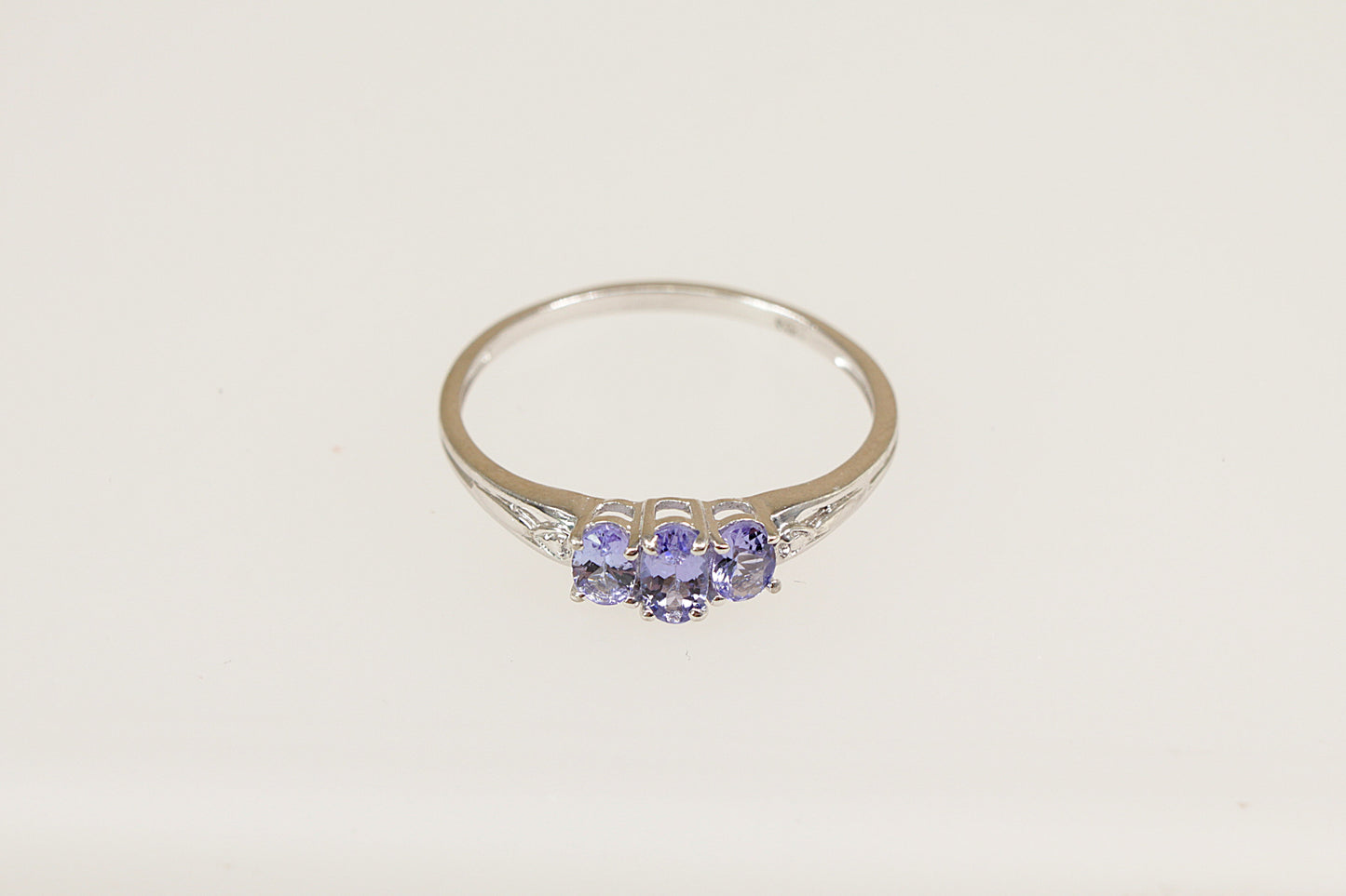 A sterling silver trilogy ring with an oval-cut tanzanite-colored crystal in the center and two smaller crystals on the sides, set in claw settings.