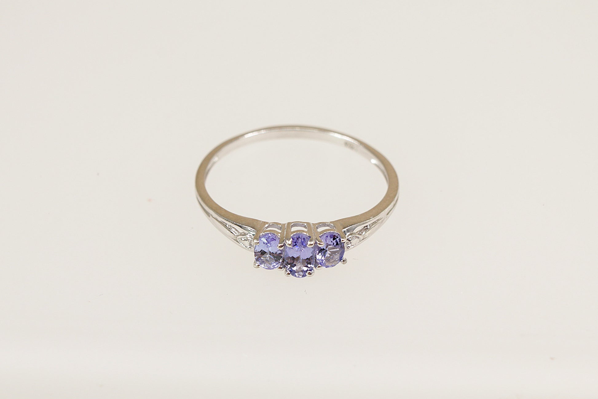 A sterling silver trilogy ring with an oval-cut tanzanite-colored crystal in the center and two smaller crystals on the sides, set in claw settings.