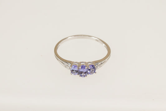 A sterling silver trilogy ring with an oval-cut tanzanite-colored crystal in the center and two smaller crystals on the sides, set in claw settings.