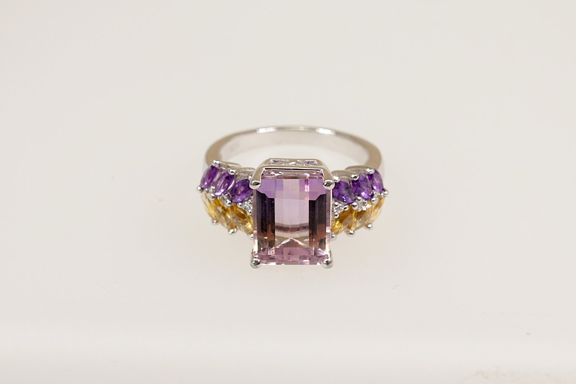 A sterling silver statement ring with an emerald-cut light amethyst center stone, flanked by marquise-cut citrines and amethysts, and set on a white background.
