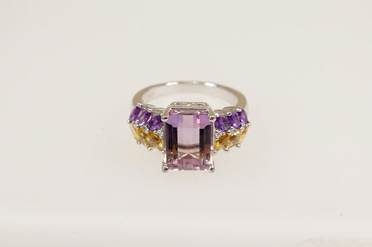 A sterling silver statement ring with an emerald-cut light amethyst center stone, flanked by marquise-cut citrines and amethysts, and set on a white background.