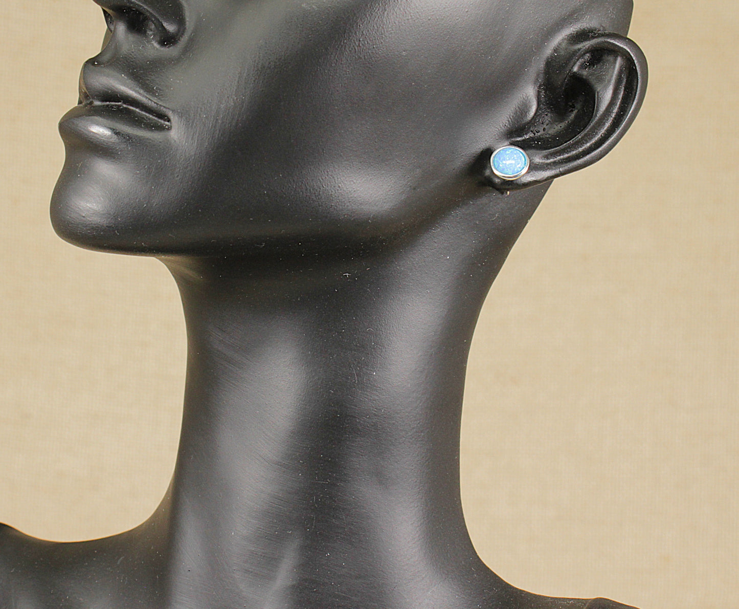 Mannequin head wearing a pair of opal stud earrings with a beige background