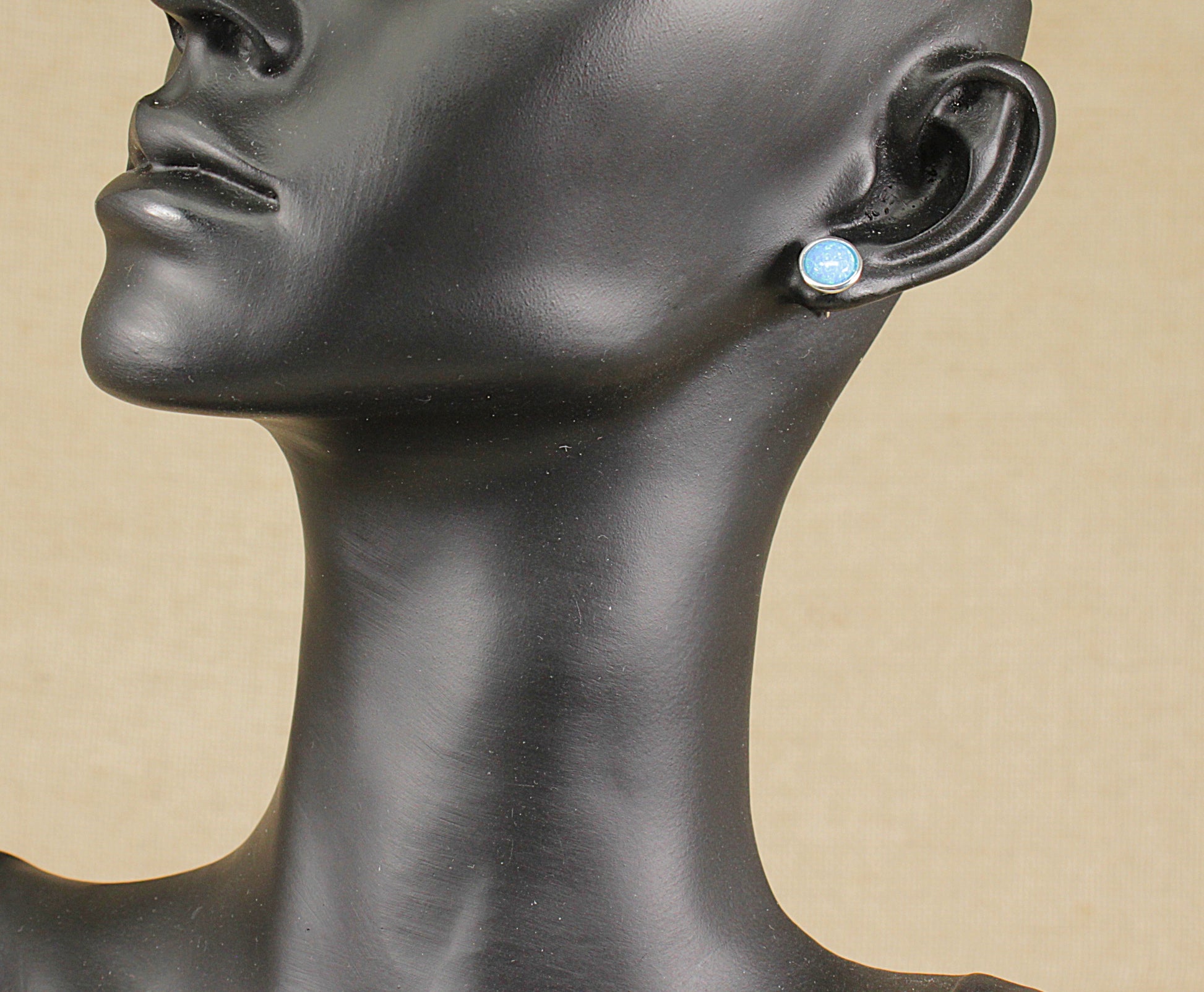 Mannequin head wearing a pair of opal stud earrings with a beige background