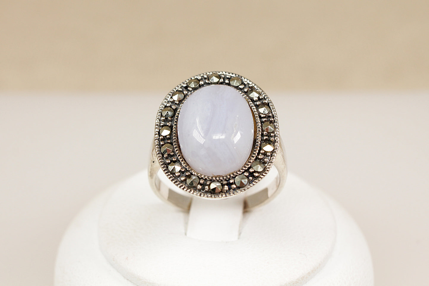 Silver ring with a large central gemstone on a white stand against a beige background