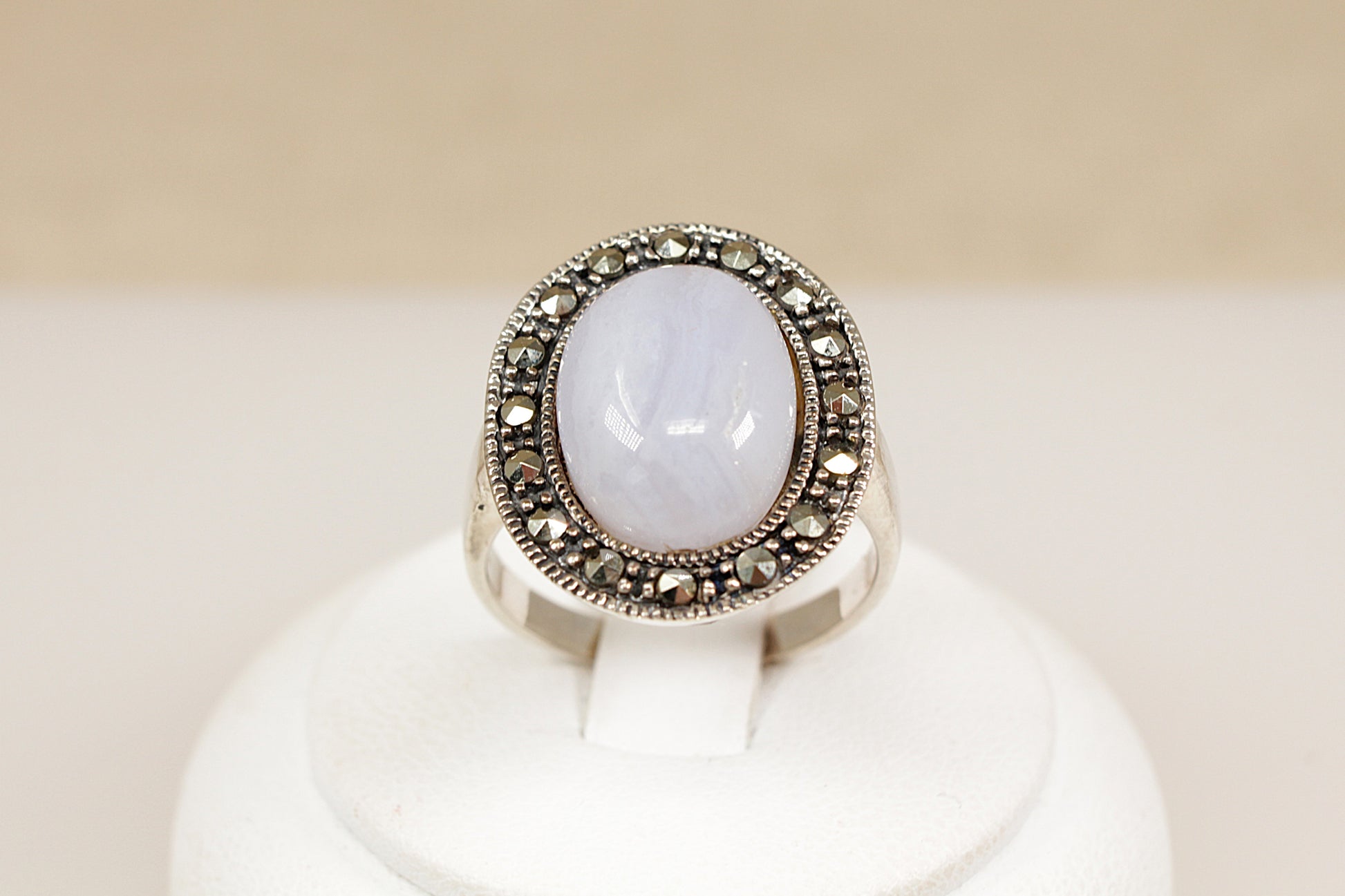 Silver ring with a large central gemstone on a white stand against a beige background