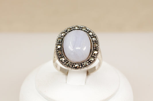 Silver ring with a large central gemstone on a white stand against a beige background