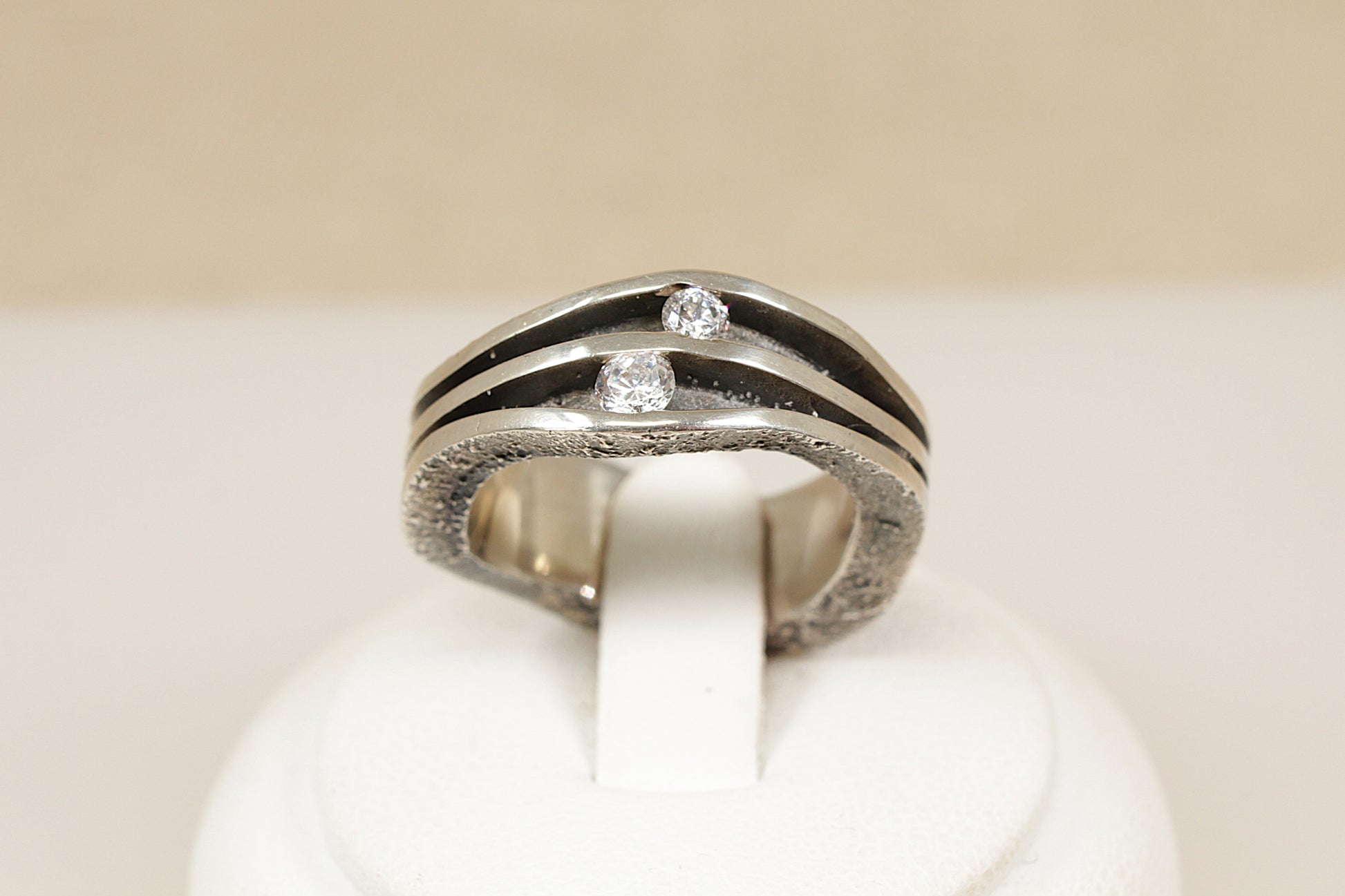 Silver ring with diamond simulant gemstones on a white stand against a beige background