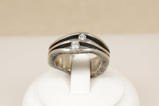Silver ring with diamond simulant gemstones on a white stand against a beige background