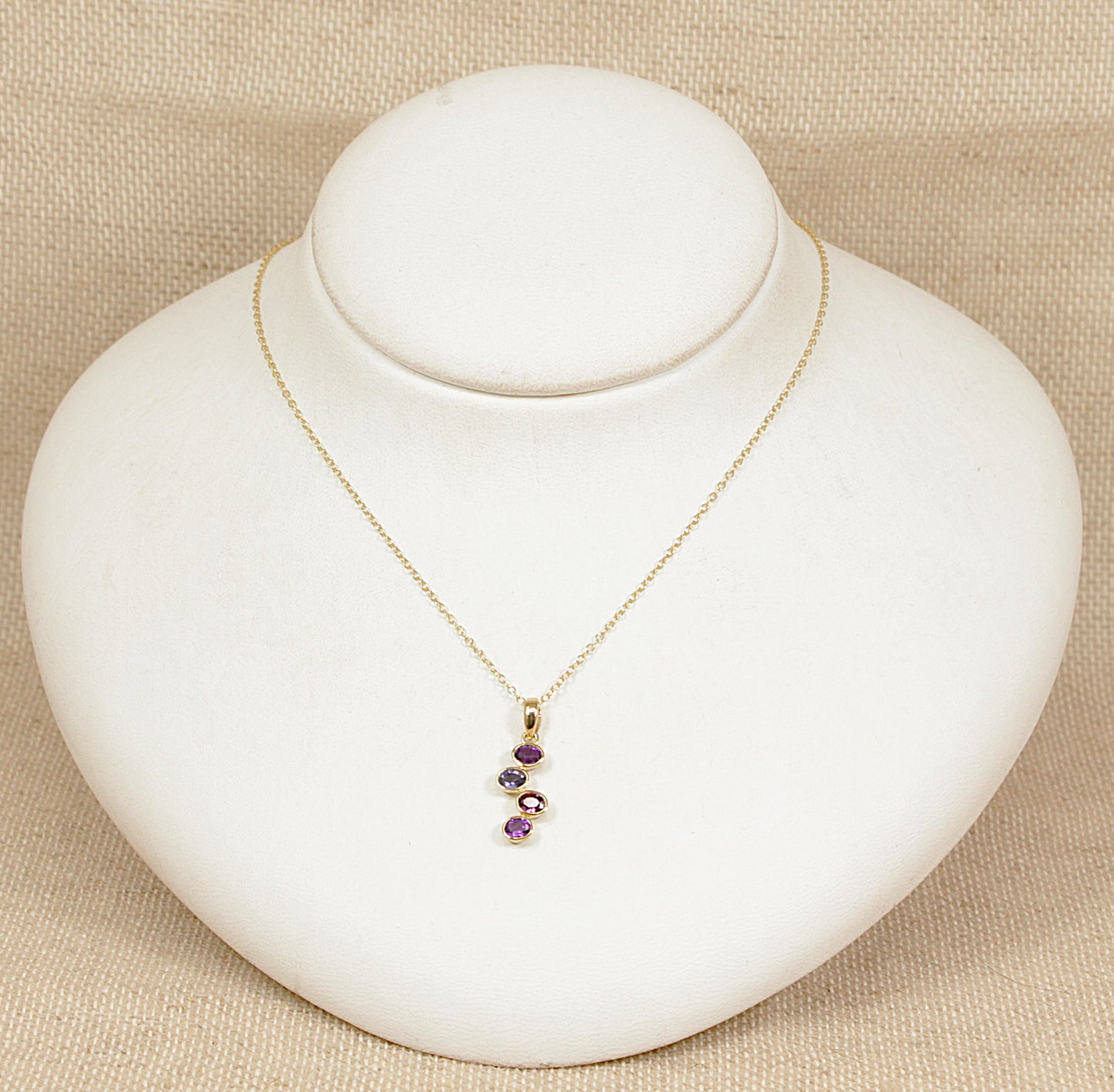 Gold necklace with amethyst garnet blue iolite gemstones on a white mannequin bust against a beige background