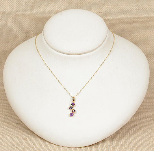 Gold necklace with amethyst garnet blue iolite gemstones on a white mannequin bust against a beige background