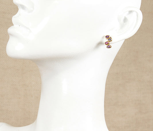 Close-up of a person wearing gold multi gemstone amethyst garnet blue iolite colorful earrings with a neutral background
