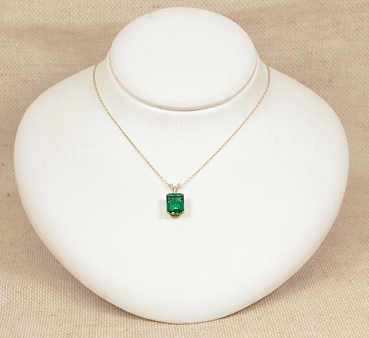 Gold necklace with a green gemstone pendant on a white stand against a beige background