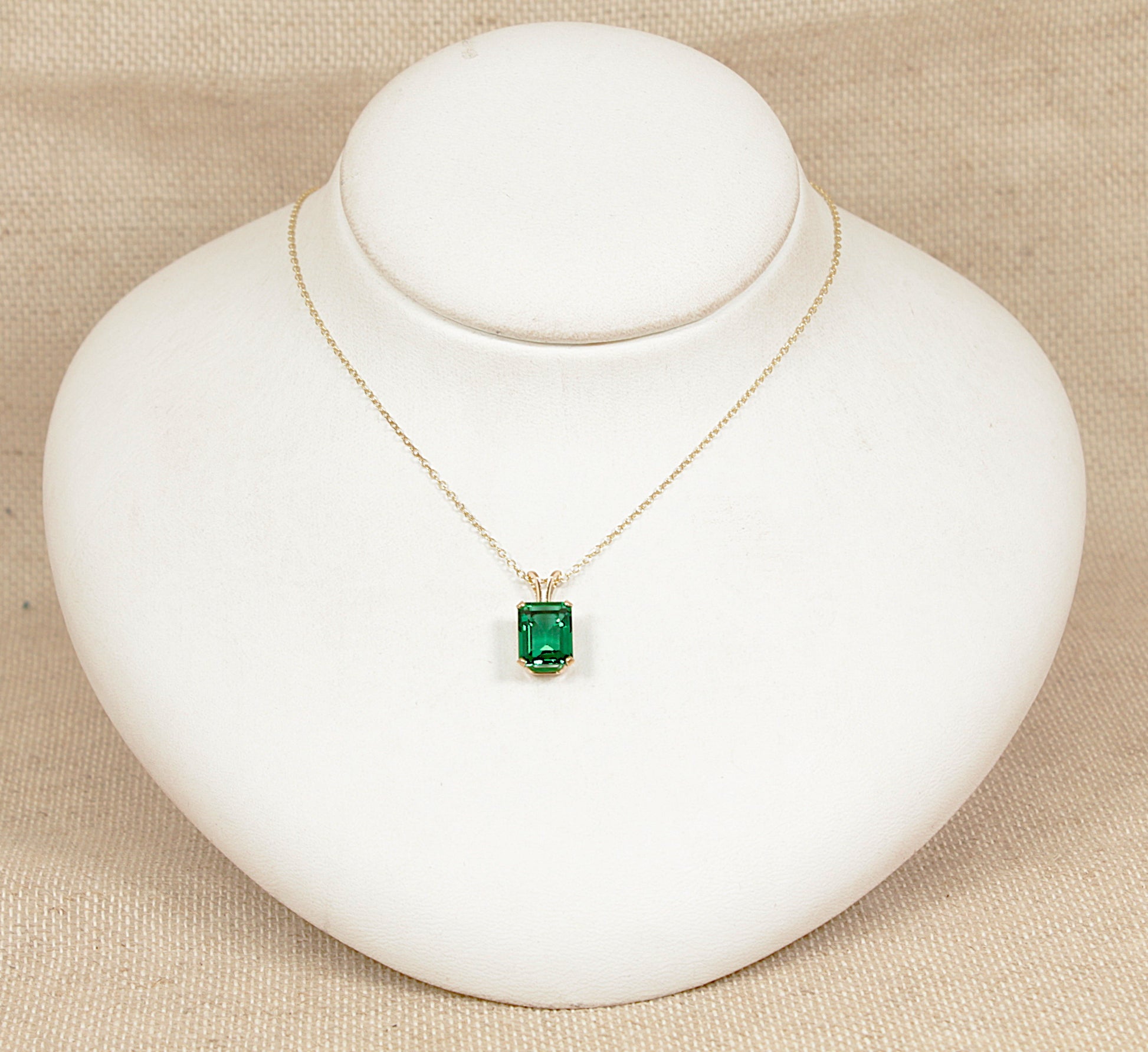 Gold necklace with a green gemstone pendant on a white stand against a beige background