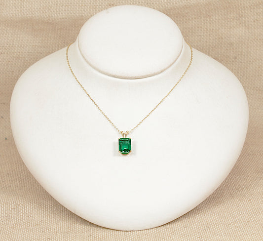 Gold necklace with a green gemstone pendant on a white stand against a beige background