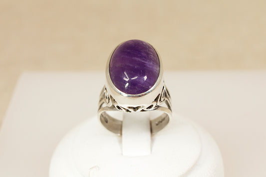 Silver ring with a purple gemstone on a white stand against a beige background