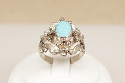 Silver ring with a light blue gemstone on a white stand against a beige background