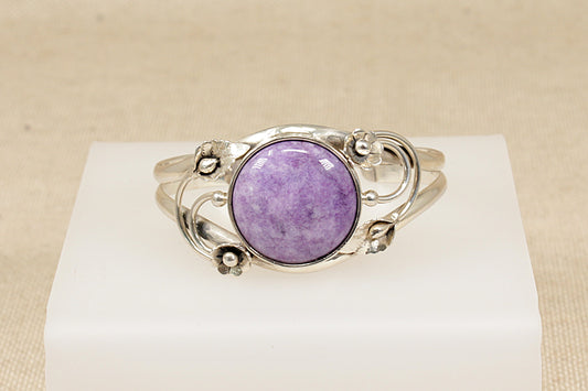 Silver bracelet with a Amethyst  gemstone on a white stand against a beige background