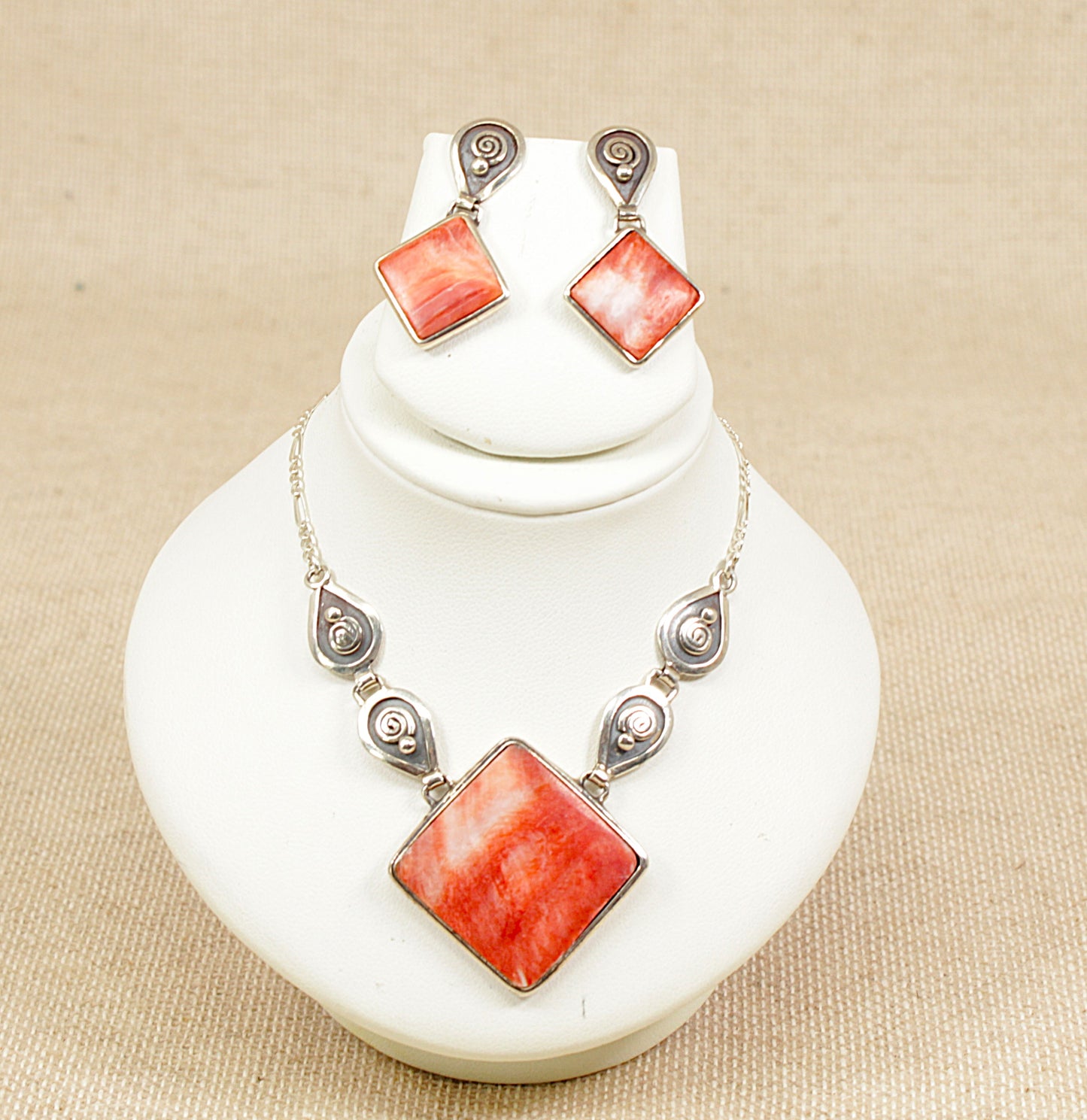 Necklace and earrings set with orange / fire square stones on a white stand.