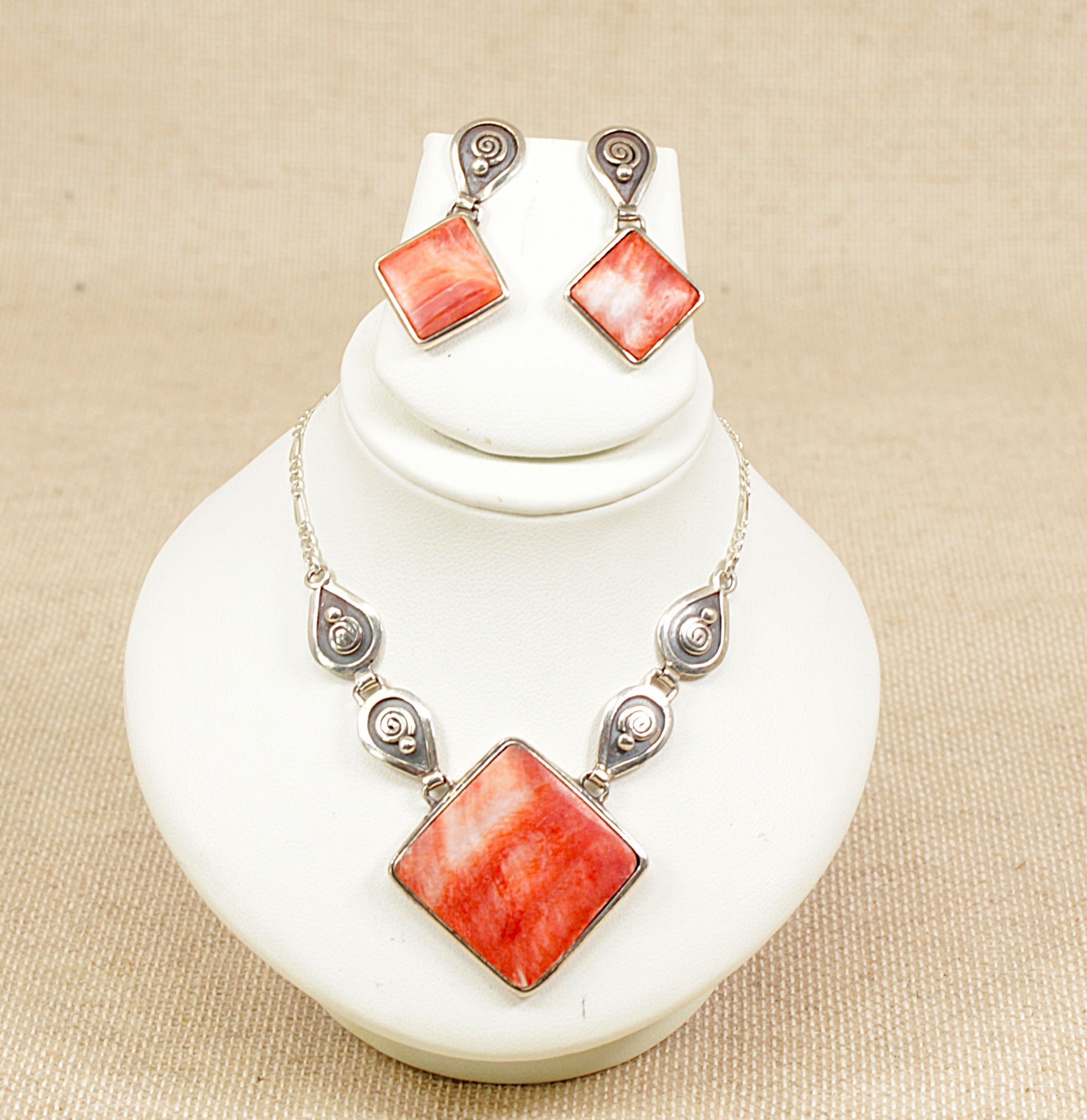 Necklace and earrings set with orange / fire square stones on a white stand.
