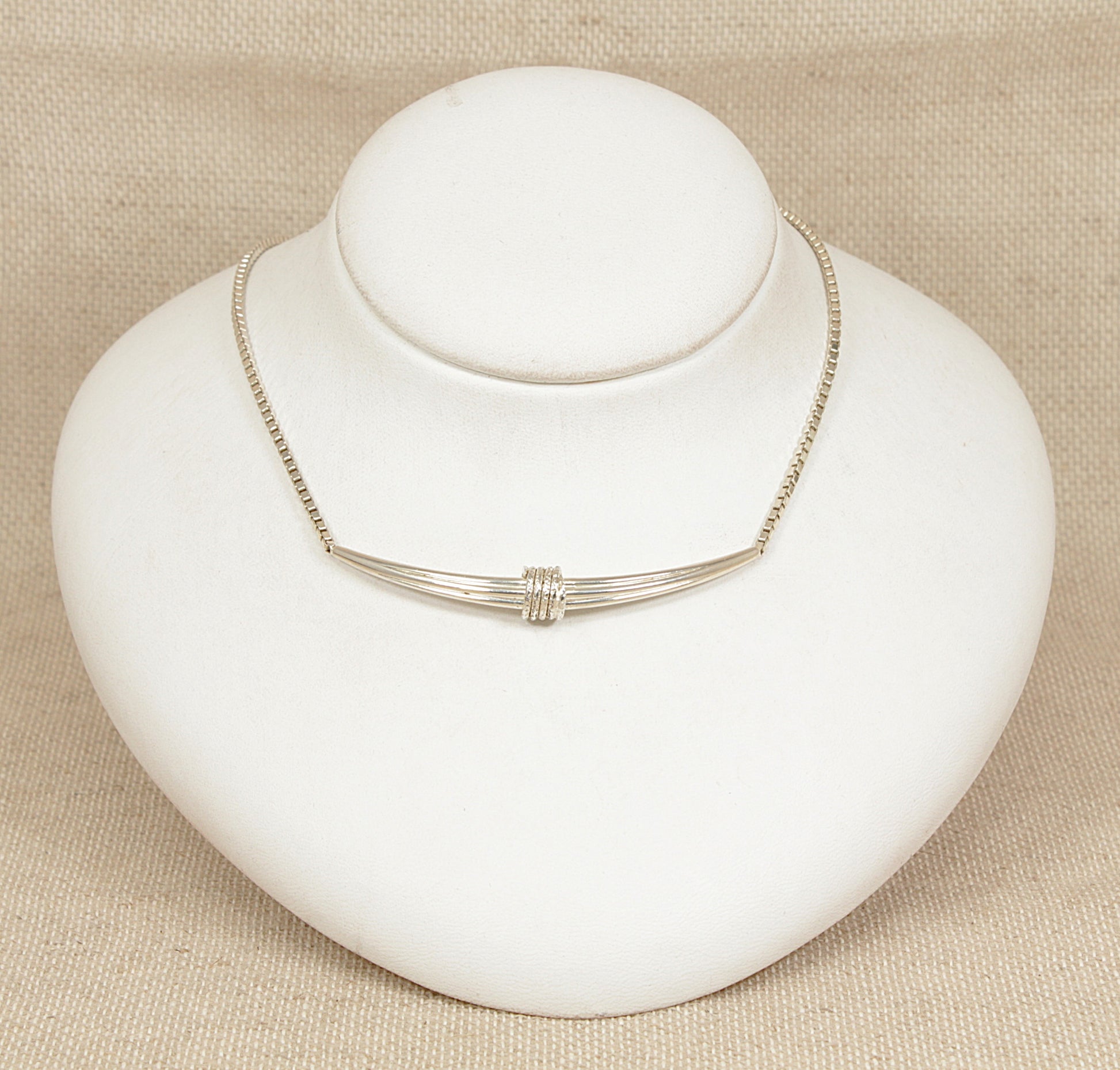 Silver necklace on a white mannequin bust against a beige background