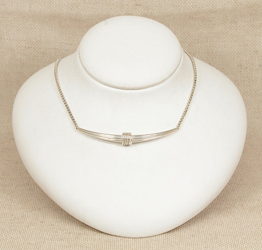 Silver necklace on a white mannequin bust against a beige background