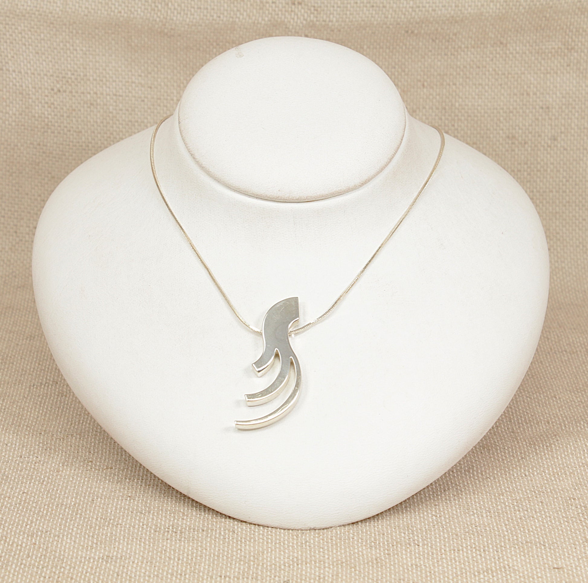 Silver necklace with a unique pendant on a white stand against a beige background