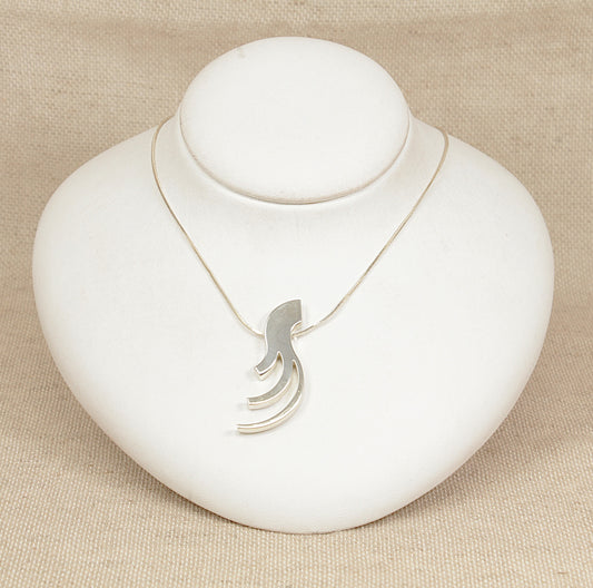 Silver necklace with a unique pendant on a white stand against a beige background