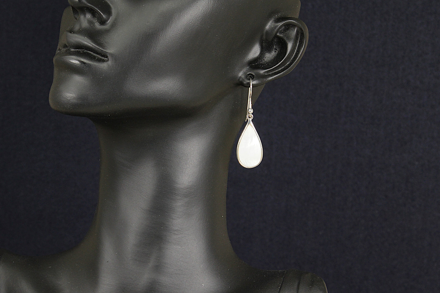 Teardrop-shaped earring on a black mannequin against a dark background