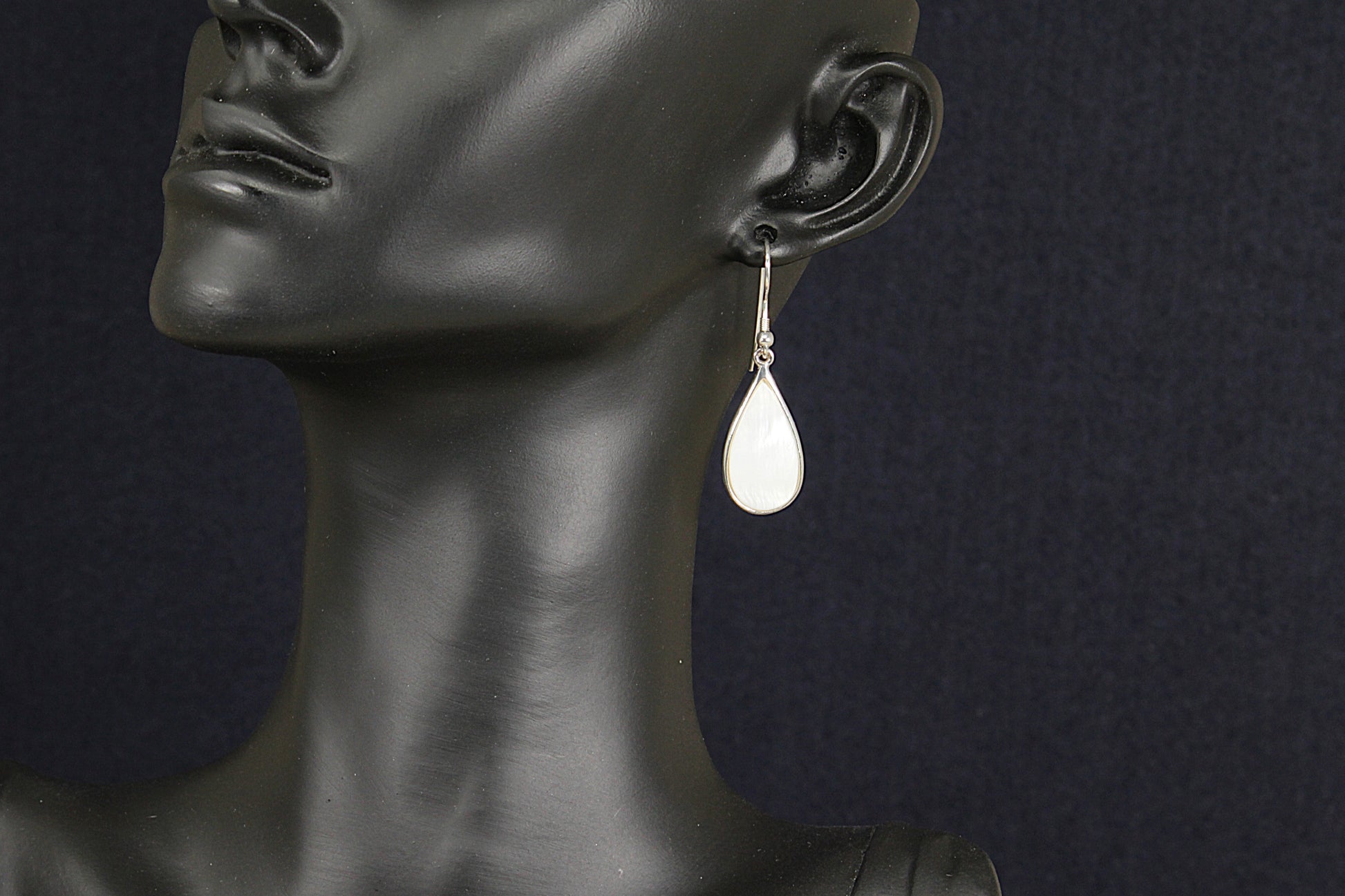 Teardrop-shaped earring on a black mannequin against a dark background