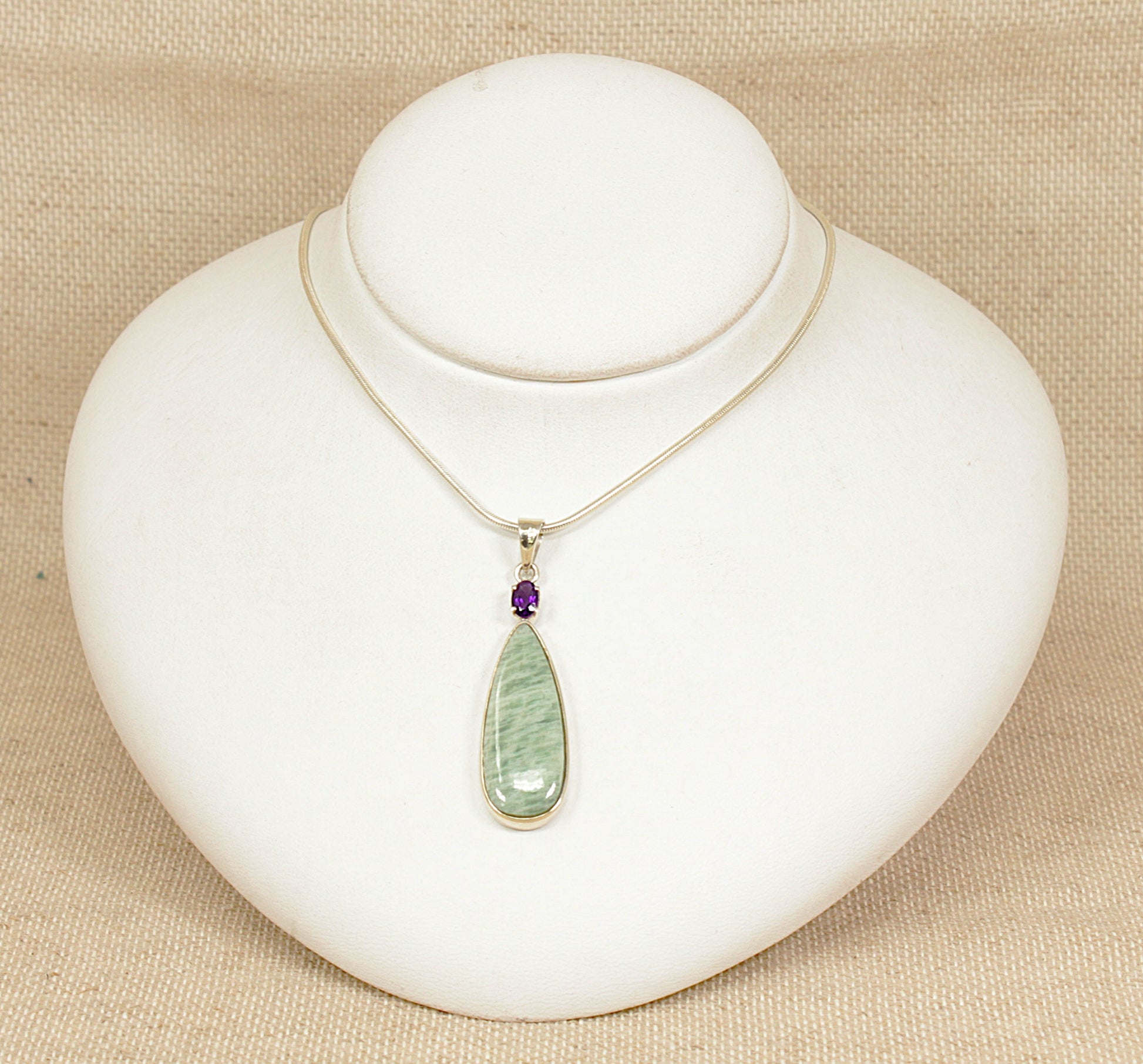 Necklace with a green pendant on a white mannequin bust against a beige background
