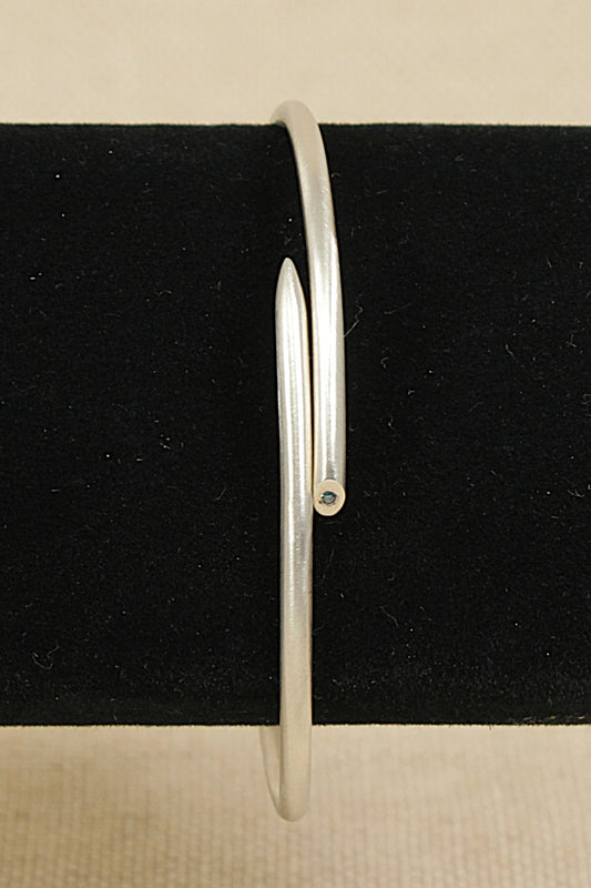 Silver bangle on a black stand with a beige background