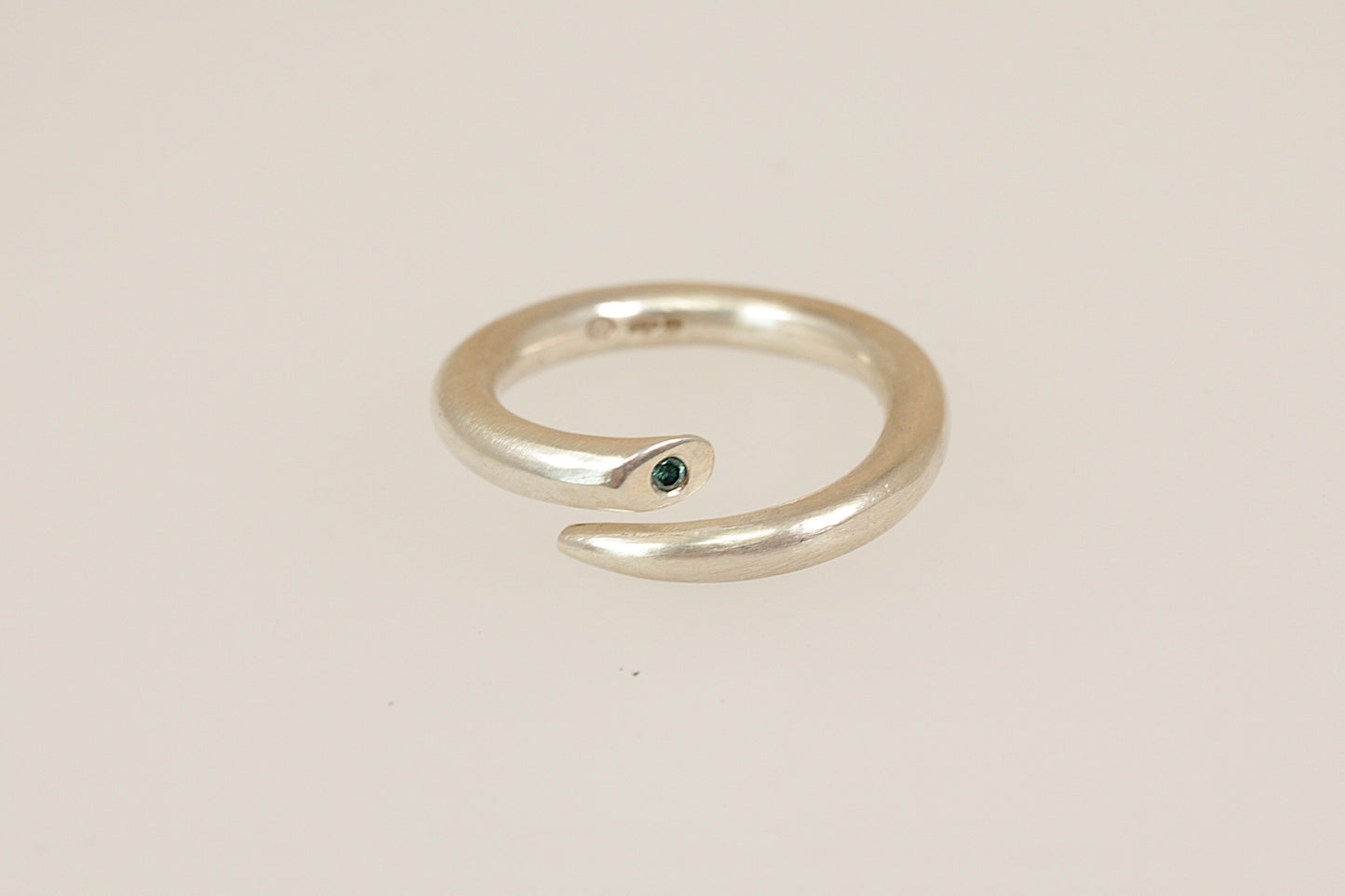 Silver ring with a small blue diamond gemstone on a beige background