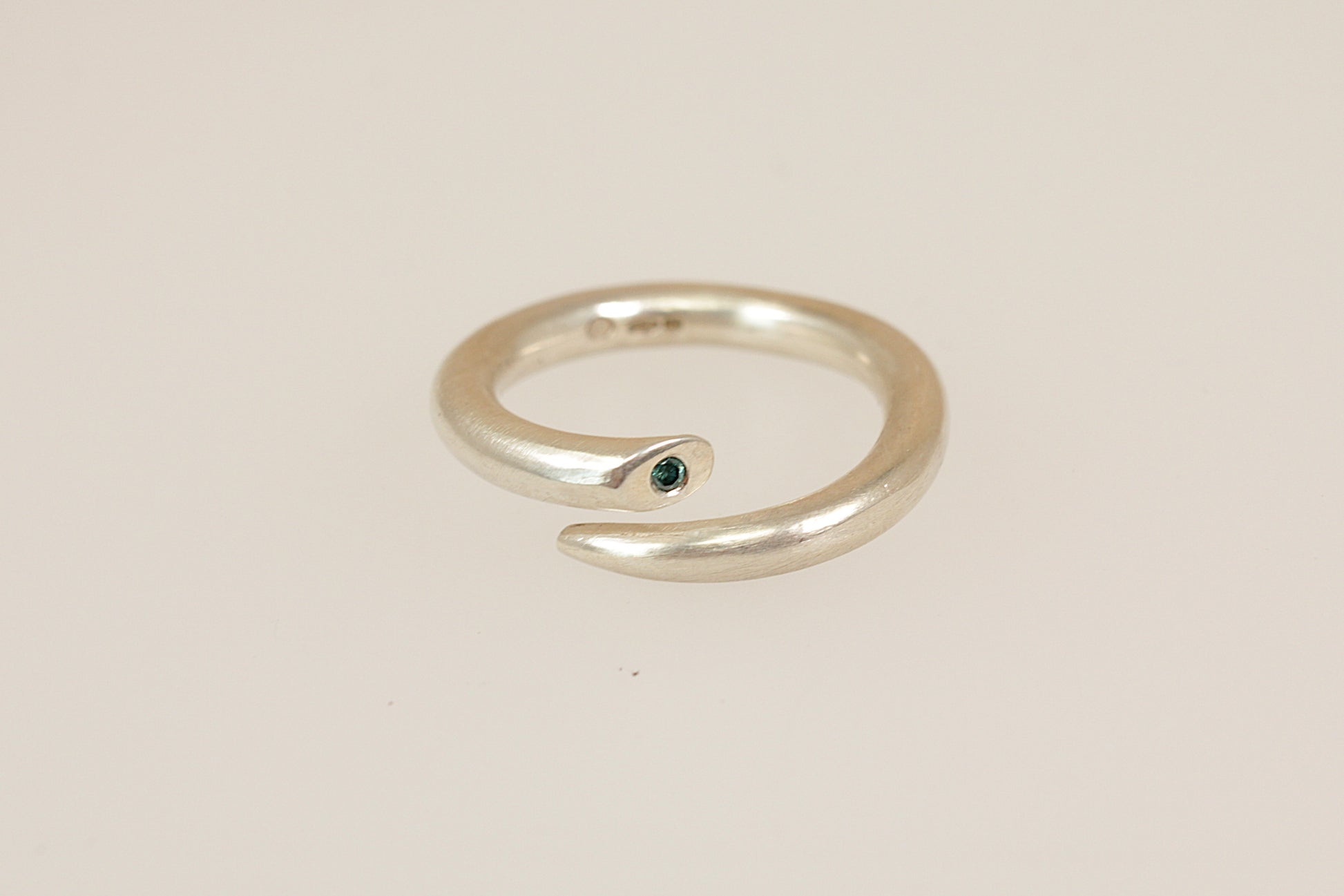 Silver ring with a small blue diamond gemstone on a beige background