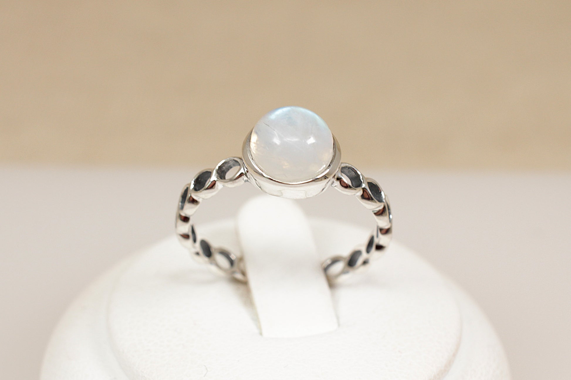 Silver ring with a round gemstone on a white stand against a beige background