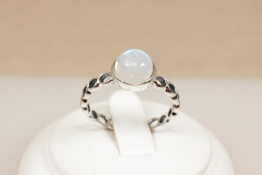 Silver ring with a round gemstone on a white stand against a beige background