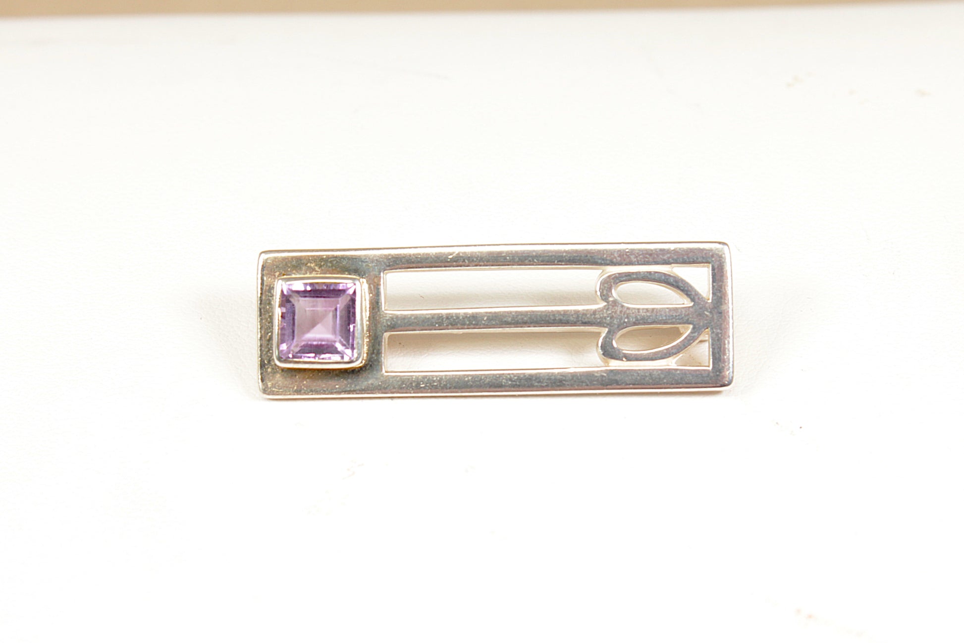 Silver brooch with a purple gemstone on a white background