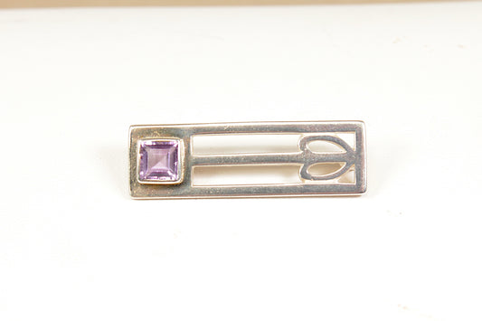 Silver brooch with a purple gemstone on a white background