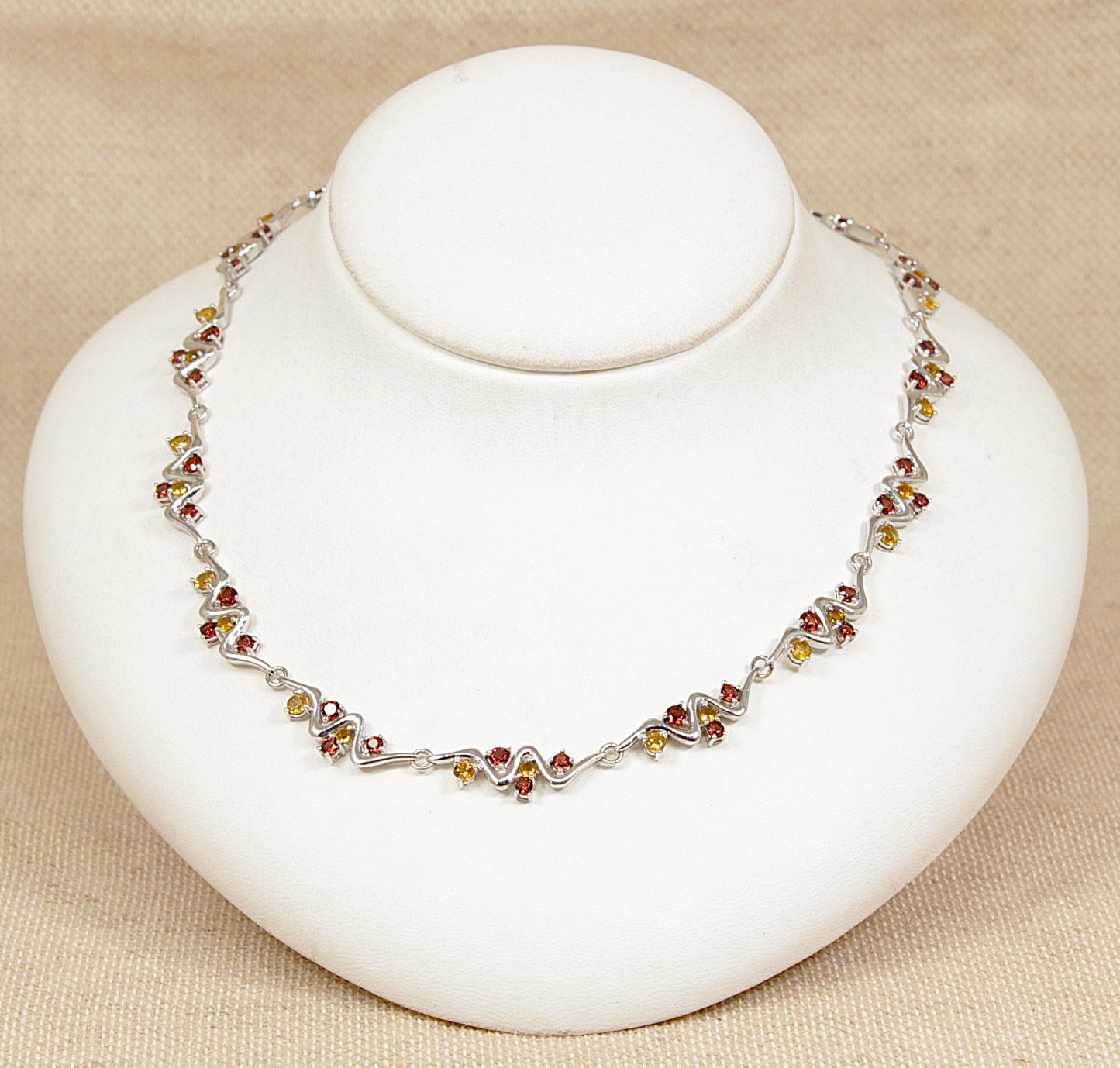 Silver necklace with multi gemstones citrine garnet on a white stand against a beige background