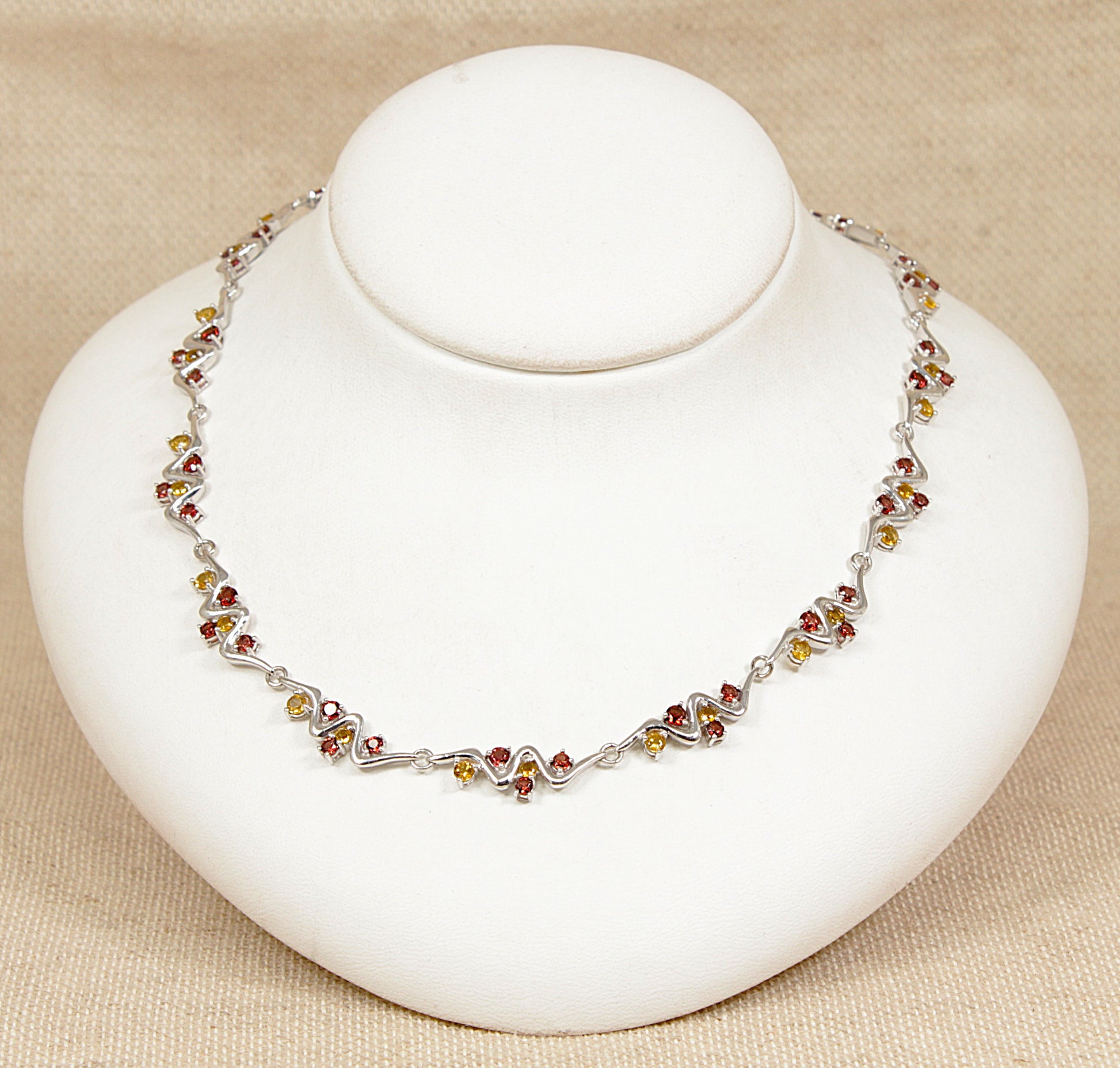 Silver necklace with multi gemstones citrine garnet on a white stand against a beige background