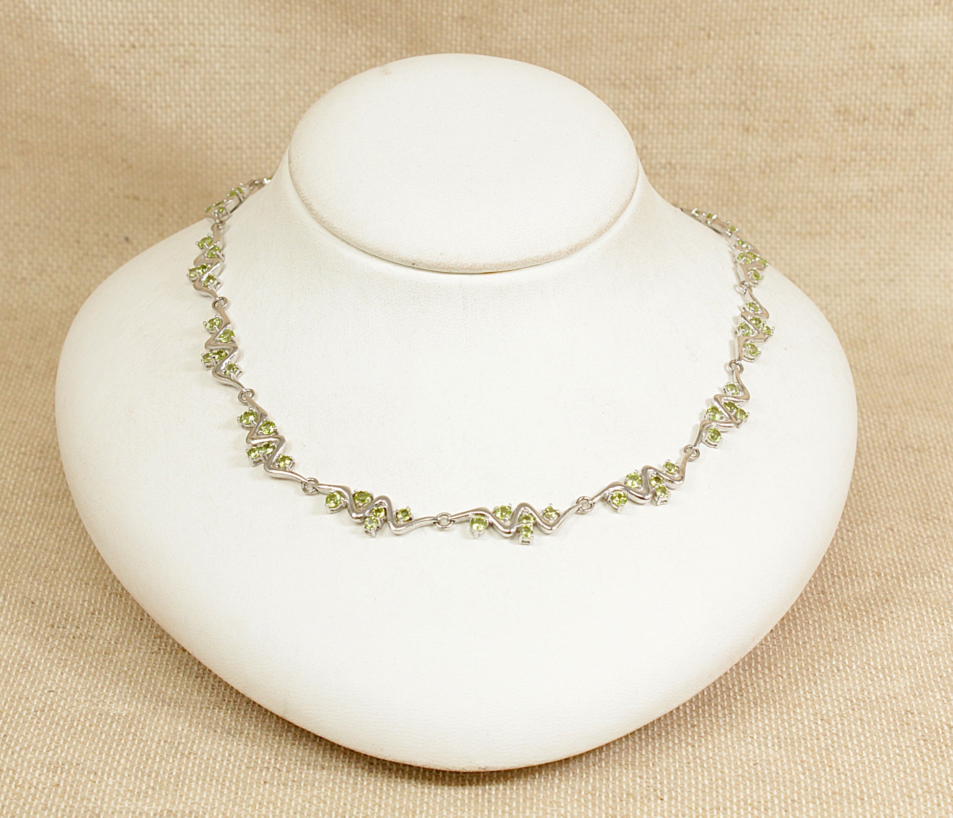 Silver peridot necklace on a white stand with a beige background