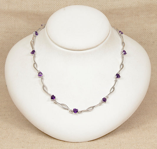 Silver necklace with purple amethyst heart shape gemstones on a white stand against a beige background